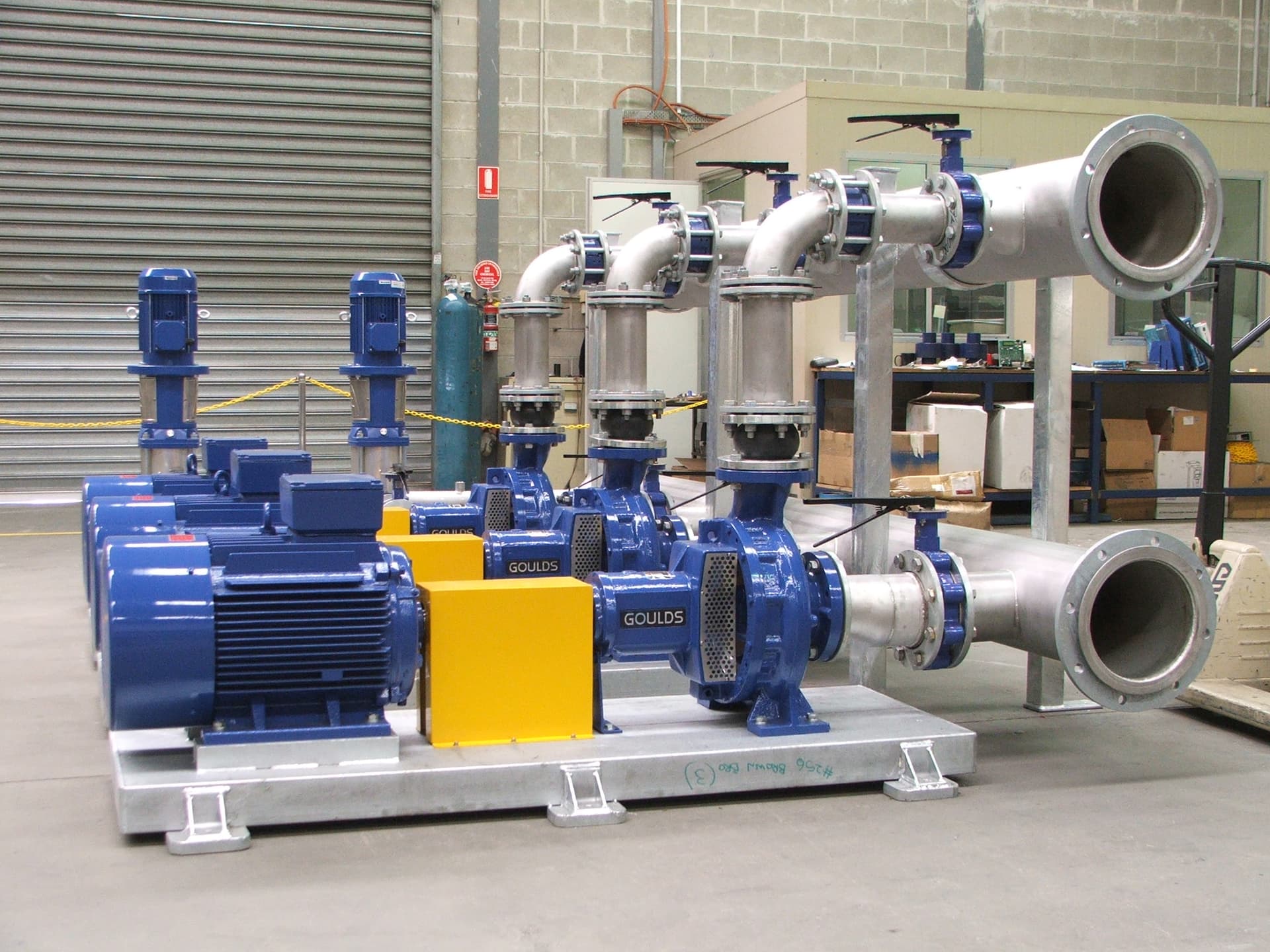 A pump skid with Goulds pumps, blue motors and stainless steel pipework in a workshop